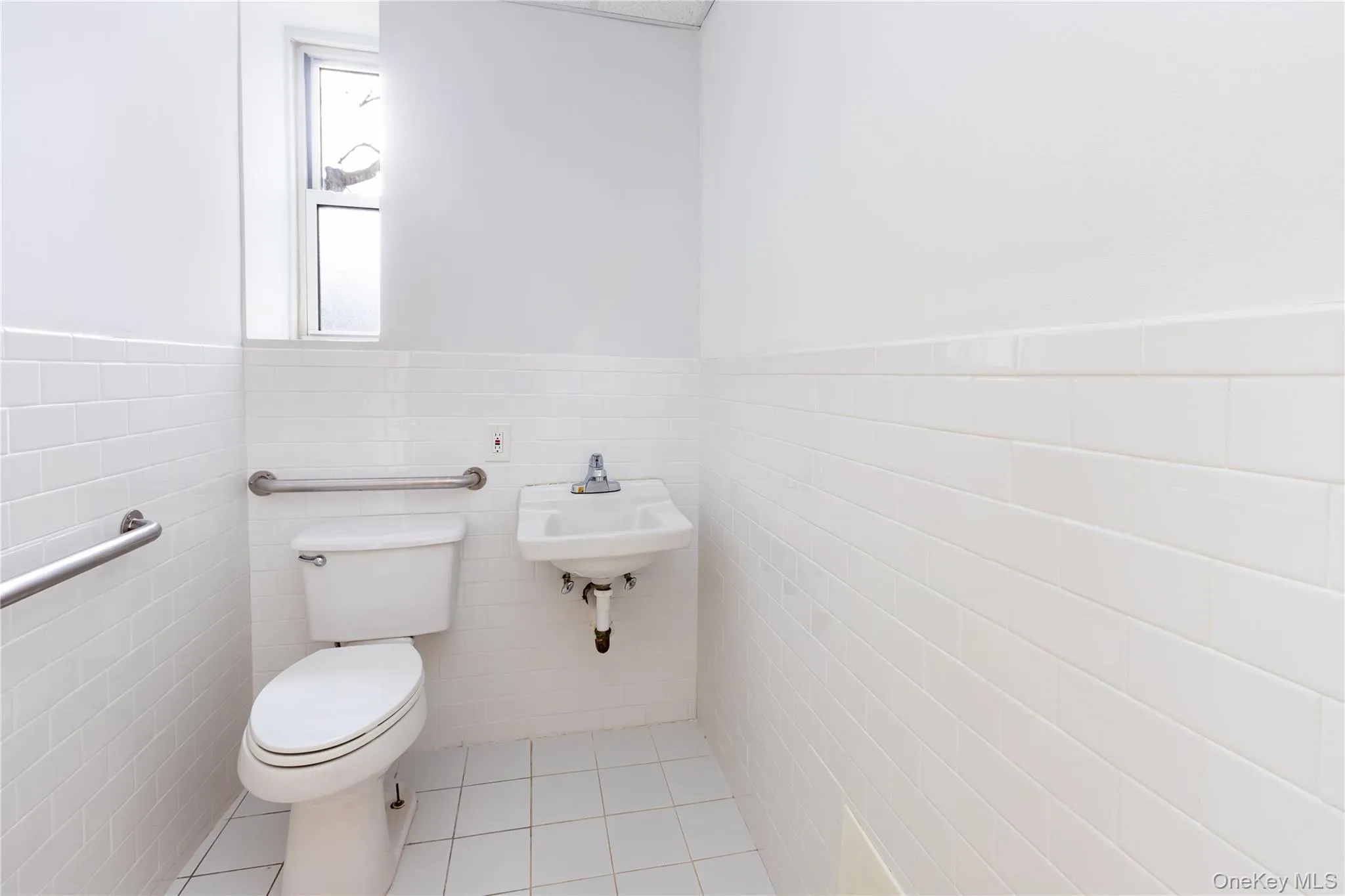 Bathroom featuring toilet, tile walls, and tile patterned flooring Bathroom featuring toilet, tile walls, and tile patterned flooring