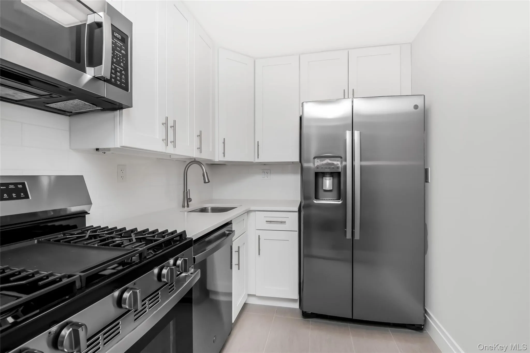 Kitchen with decorative backsplash, white cabinetry, a sink, and appliances with stainless steel finishes Kitchen with decorative backsplash, white cabinetry, a sink, and appliances with stainless steel finishes