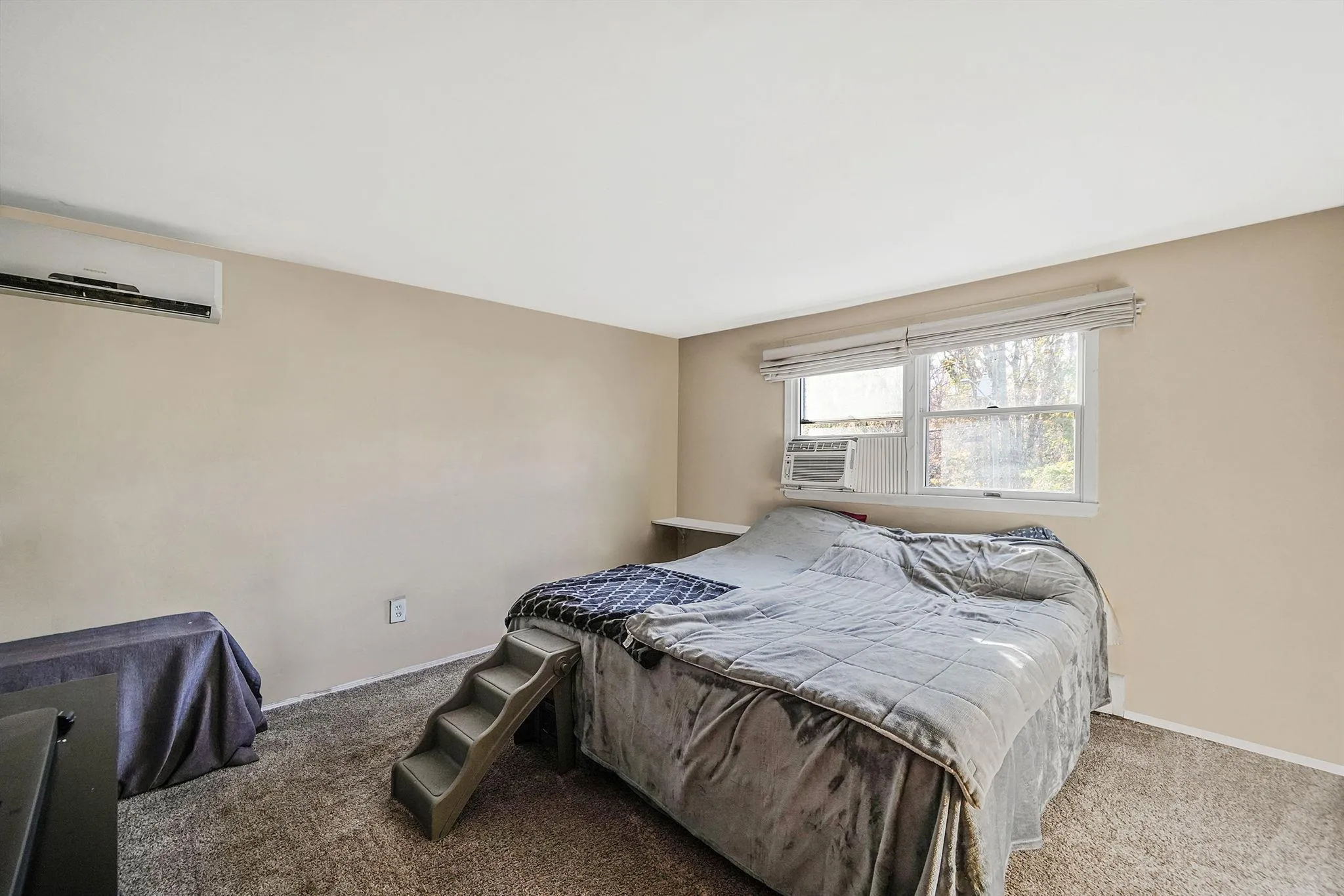 Carpeted bedroom featuring an AC wall unit and baseboards Carpeted bedroom featuring an AC wall unit and baseboards