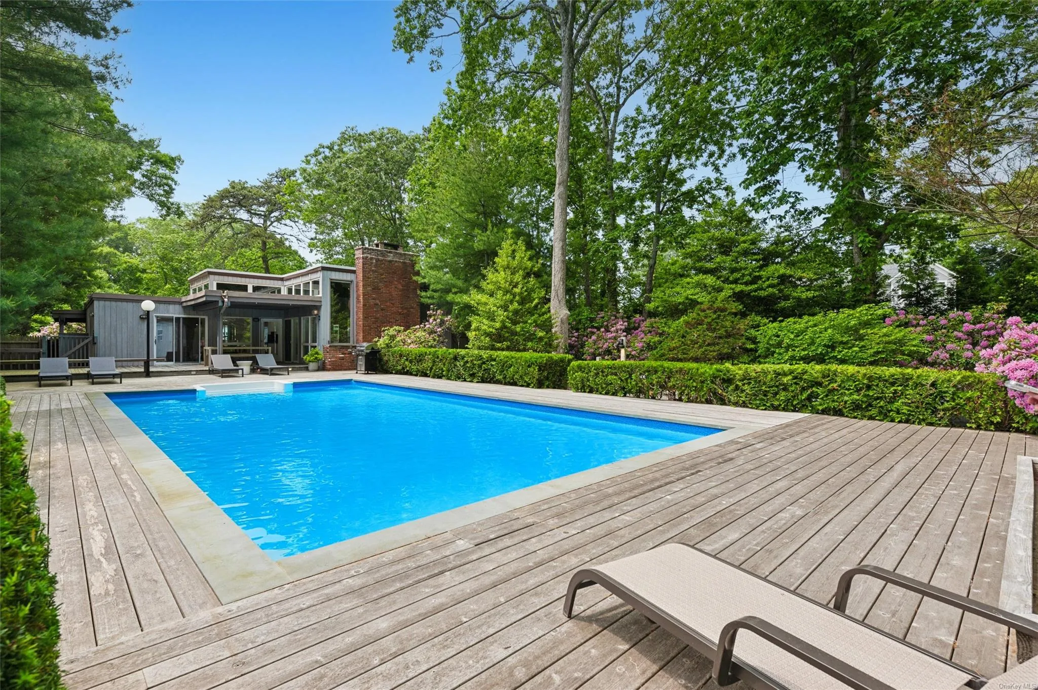 Swimming pool featuring a sunroom, a wooden deck, and view of scattered trees Swimming pool featuring a sunroom, a wooden deck, and view of scattered trees