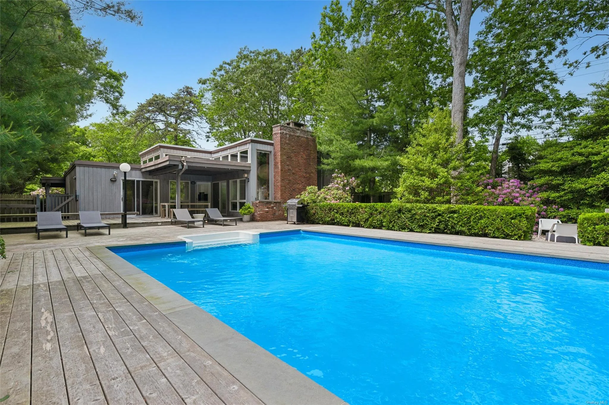 Outdoor pool featuring view of scattered trees, a sunroom, and a deck Outdoor pool featuring view of scattered trees, a sunroom, and a deck