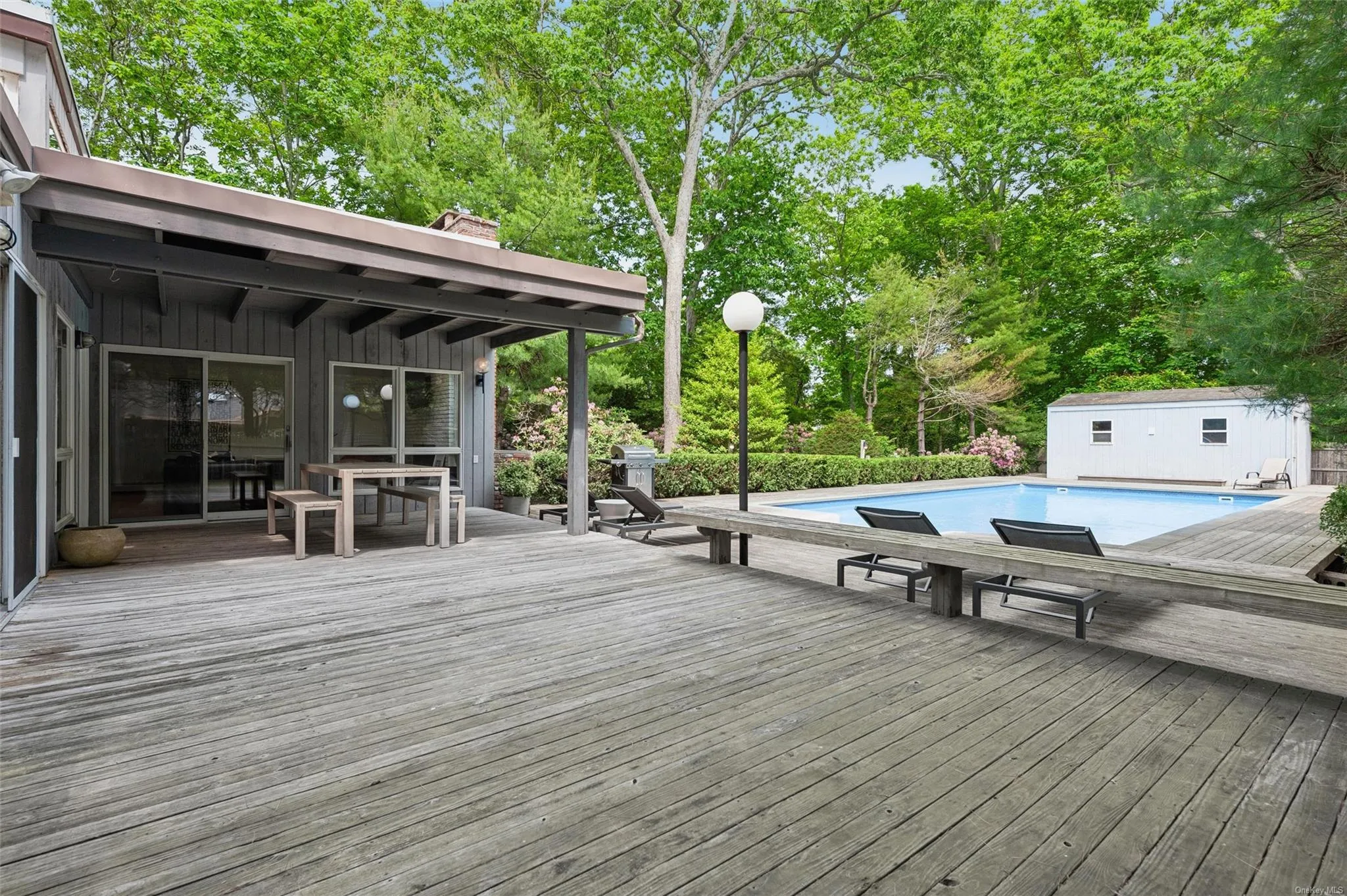 Wooden terrace with an outdoor pool, outdoor dining space, view of scattered trees, and an outbuilding Wooden terrace with an outdoor pool, outdoor dining space, view of scattered trees, and an outbuilding