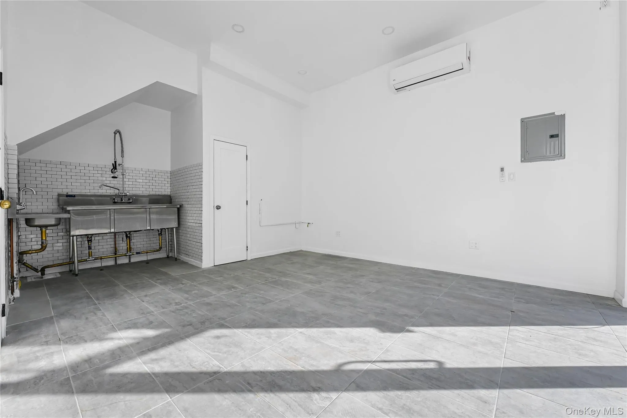 Unfurnished living room with electric panel, an AC wall unit, sink, and brick wall Unfurnished living room with electric panel, an AC wall unit, sink, and brick wall