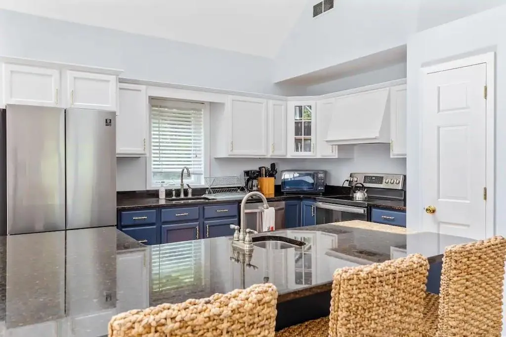 Kitchen featuring lofted ceiling, blue cabinets, custom range hood, appliances with stainless steel finishes, and white cabinetry Kitchen featuring lofted ceiling, blue cabinets, custom range hood, appliances with stainless steel finishes, and white cabinetry