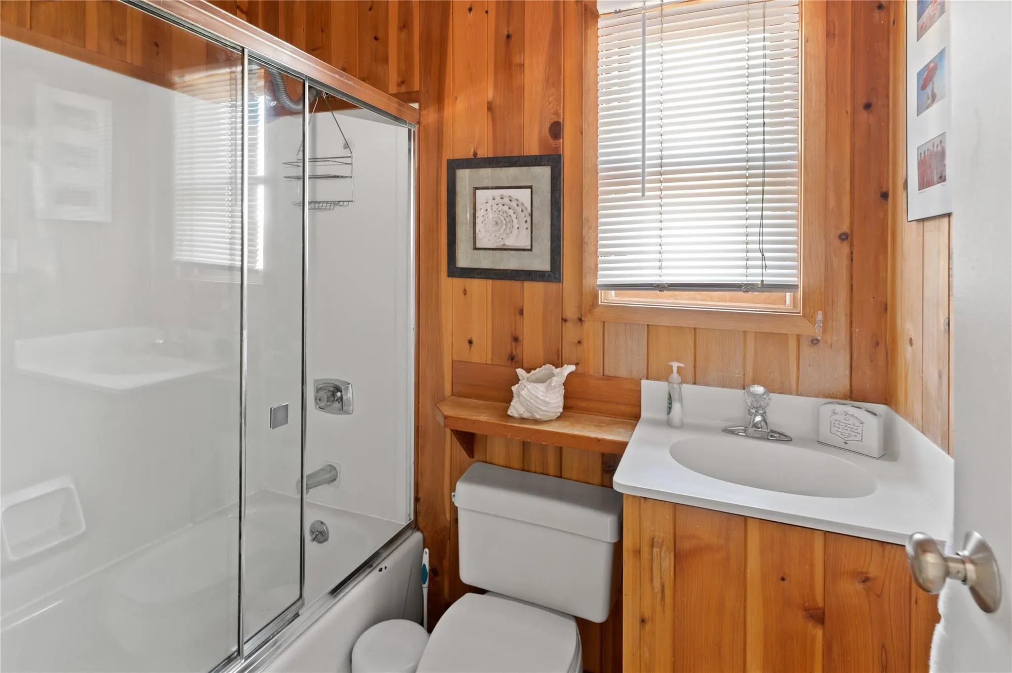 Full bathroom featuring combined bath / shower with glass door, toilet, a wealth of natural light, and wood walls Full bathroom featuring combined bath / shower with glass door, toilet, a wealth of natural light, and wood walls