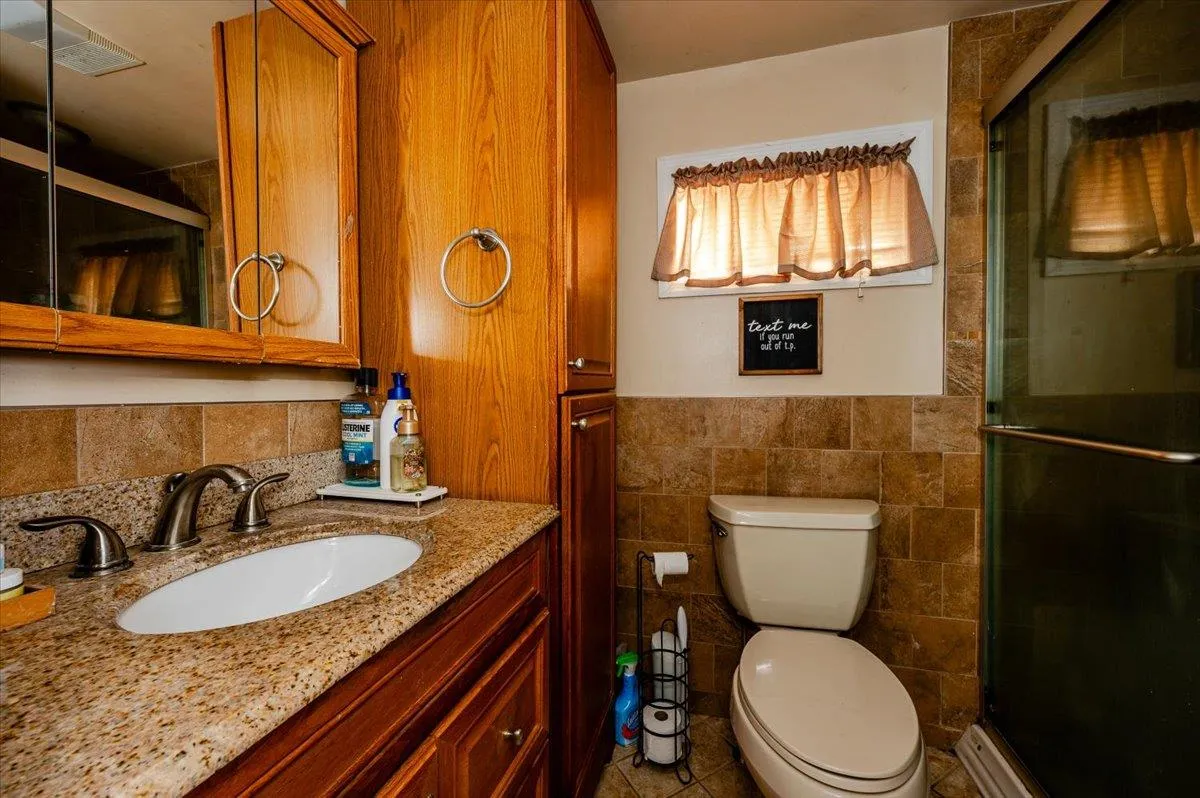 Bathroom featuring an enclosed shower, vanity, toilet, and tile walls Bathroom featuring an enclosed shower, vanity, toilet, and tile walls