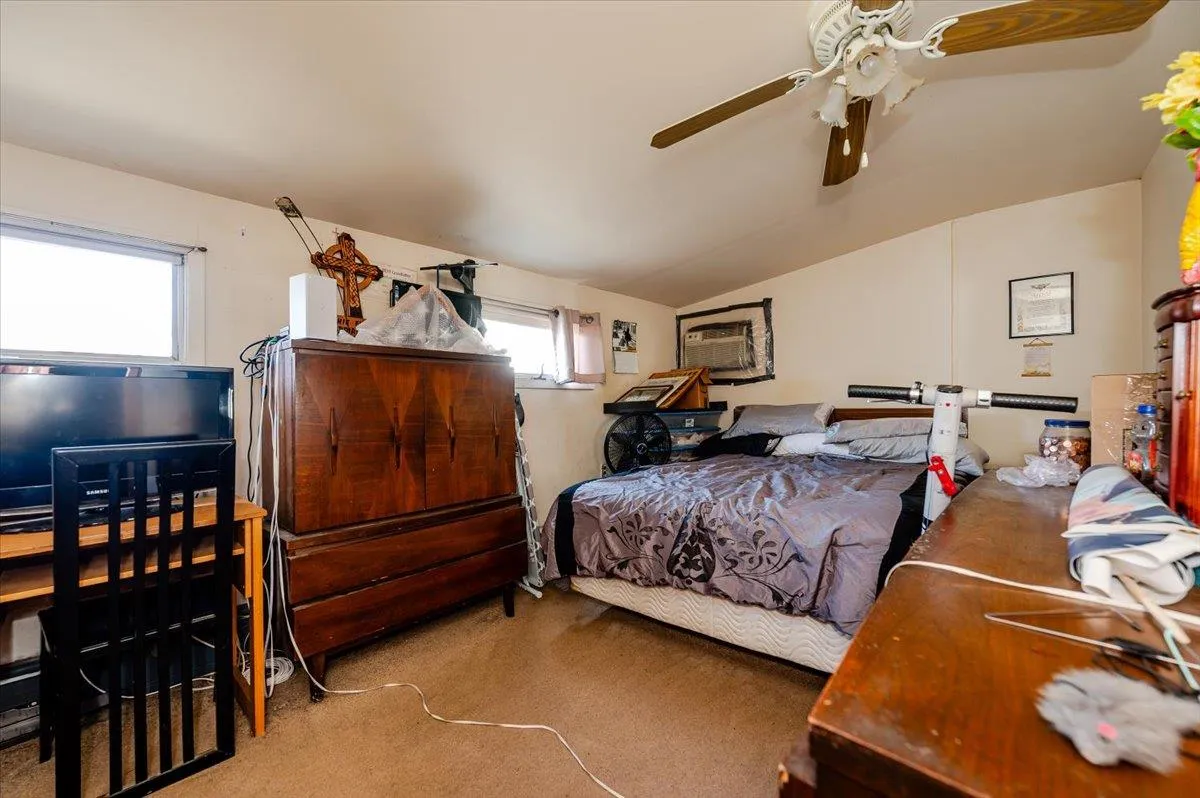 Carpeted bedroom featuring an AC wall unit, multiple windows, ceiling fan, and vaulted ceiling Carpeted bedroom featuring an AC wall unit, multiple windows, ceiling fan, and vaulted ceiling