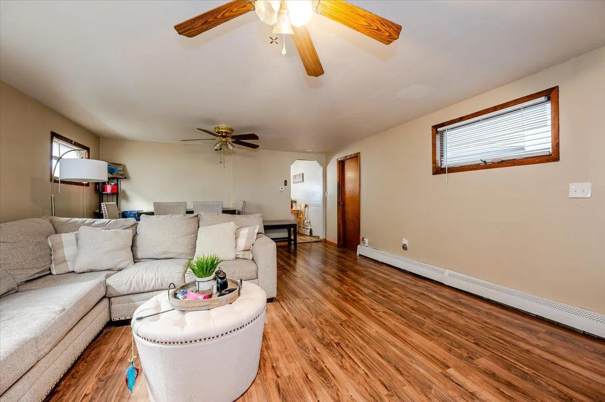 Living room featuring wood-type flooring, ceiling fan, and a baseboard heating unit Living room featuring wood-type flooring, ceiling fan, and a baseboard heating unit