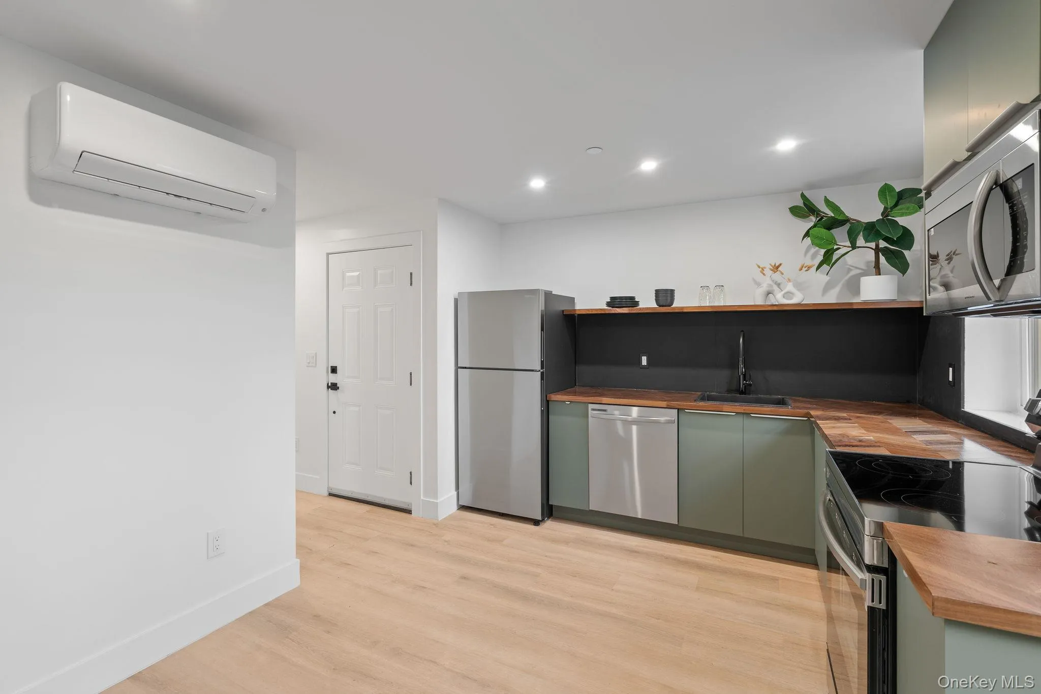 Kitchen featuring stainless steel appliances, sink, an AC wall unit, light hardwood / wood-style flooring, and butcher block counters Kitchen featuring stainless steel appliances, sink, an AC wall unit, light hardwood / wood-style flooring, and butcher block counters
