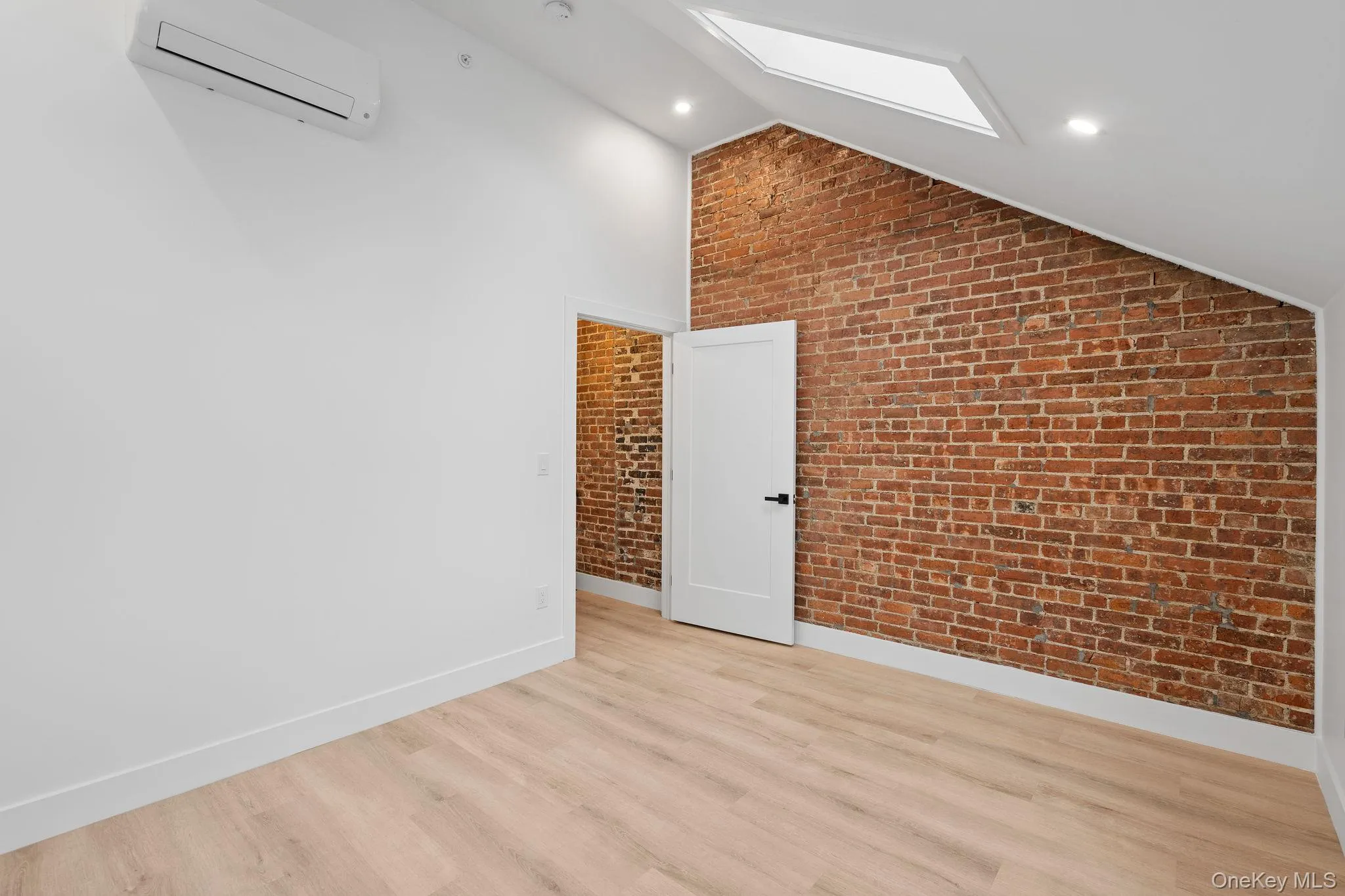 Bonus room with light hardwood / wood-style floors, lofted ceiling with skylight, a wall mounted AC, and brick wall Bonus room with light hardwood / wood-style floors, lofted ceiling with skylight, a wall mounted AC, and brick wall