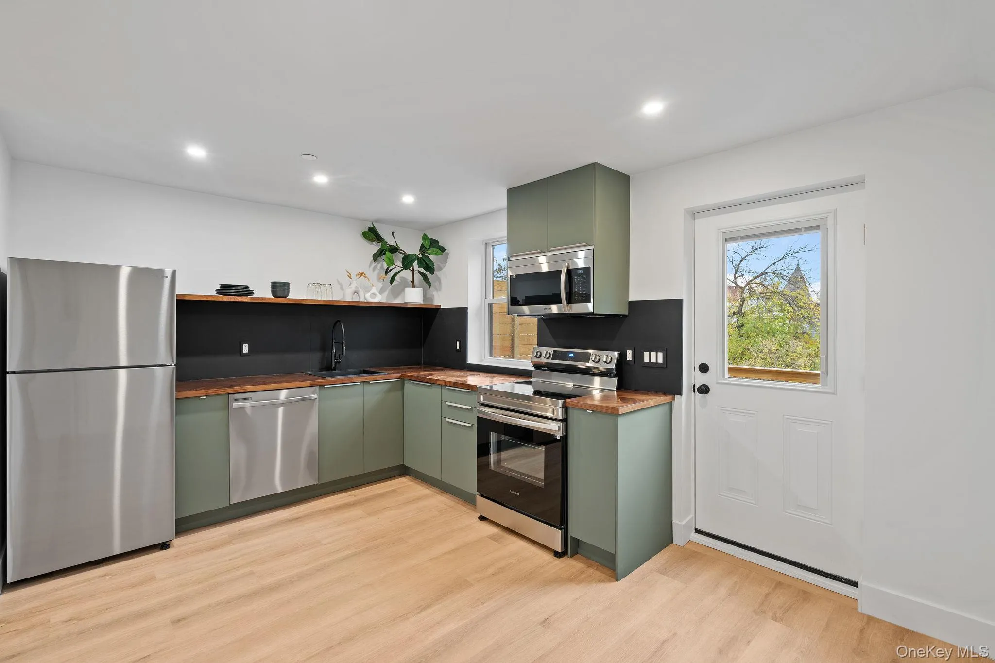Kitchen with light hardwood / wood-style floors, stainless steel appliances, butcher block counters, and green cabinetry Kitchen with light hardwood / wood-style floors, stainless steel appliances, butcher block counters, and green cabinetry