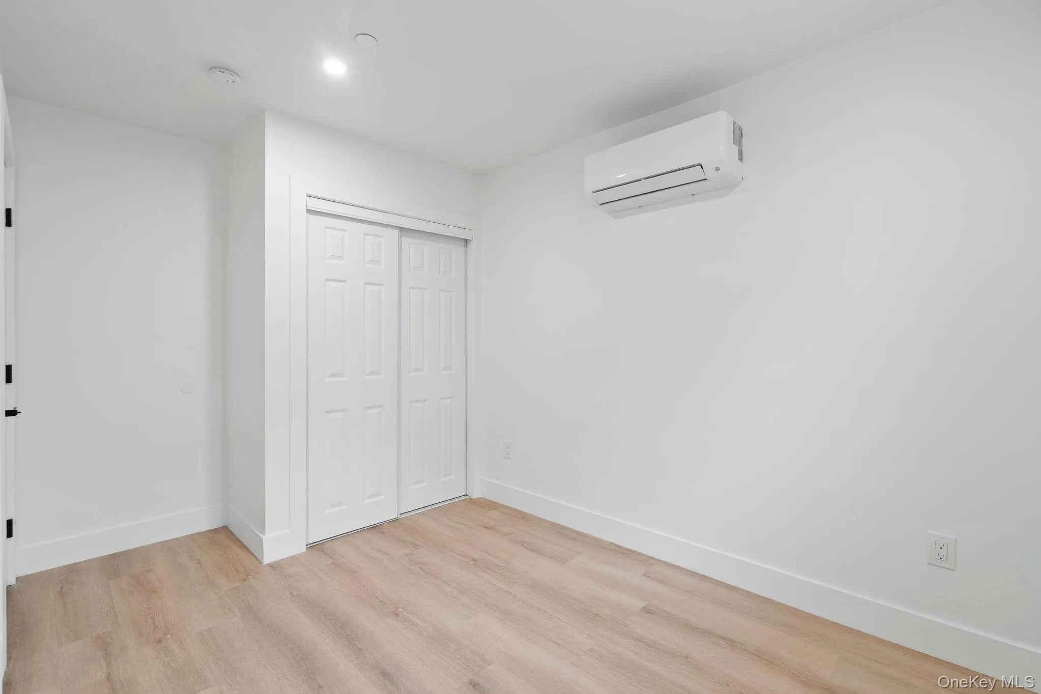 Unfurnished bedroom featuring an AC wall unit, a closet, and light wood-type flooring Unfurnished bedroom featuring an AC wall unit, a closet, and light wood-type flooring
