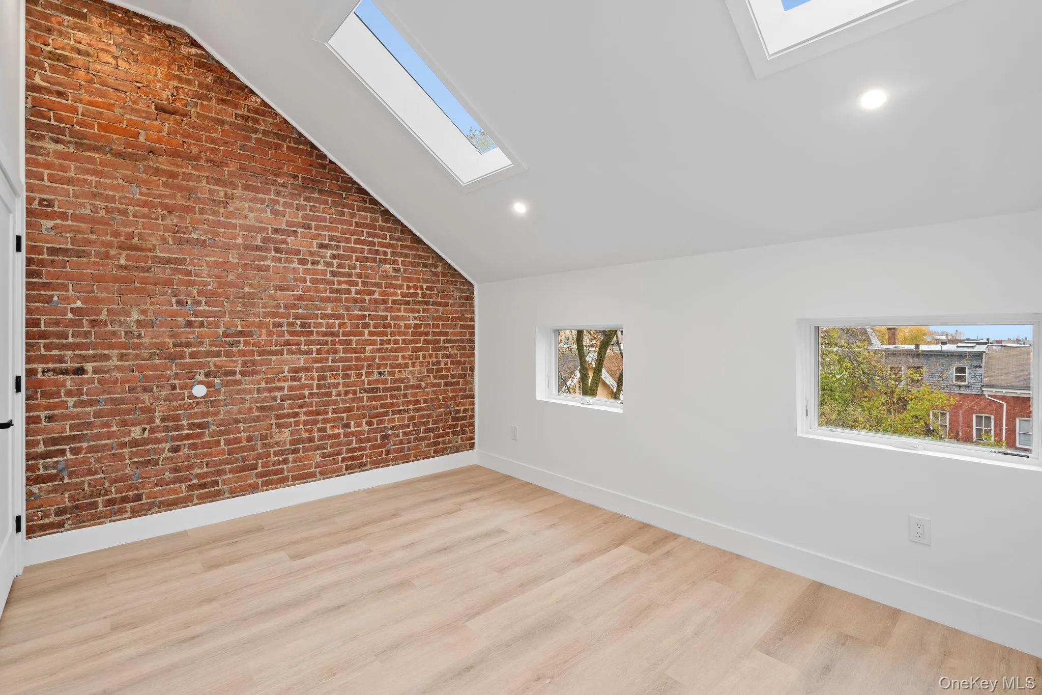 Additional living space with vaulted ceiling with skylight, light hardwood / wood-style floors, and brick wall Additional living space with vaulted ceiling with skylight, light hardwood / wood-style floors, and brick wall