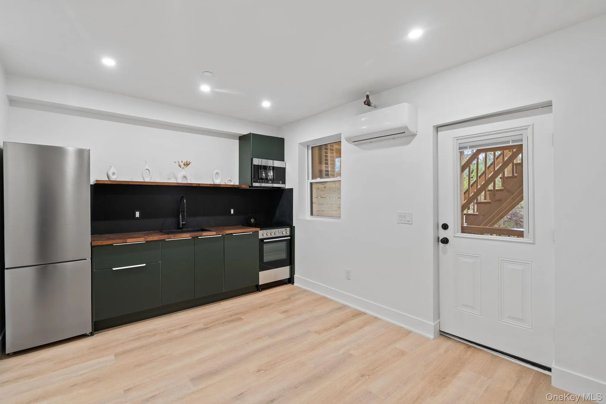 Kitchen featuring light wood-type flooring, stainless steel appliances, a wall unit AC, sink, and green cabinetry Kitchen featuring light wood-type flooring, stainless steel appliances, a wall unit AC, sink, and green cabinetry