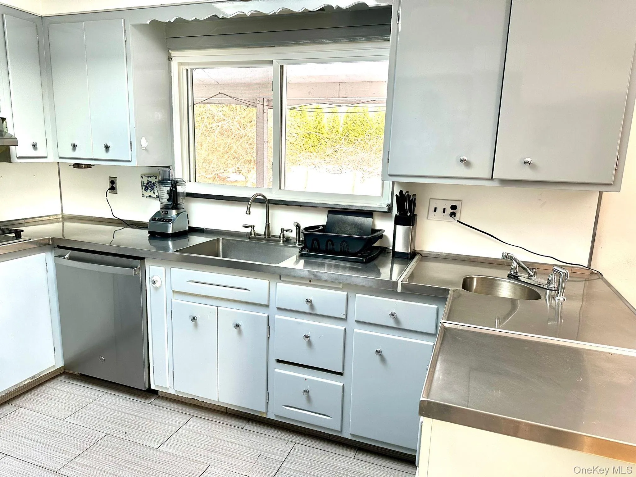 Kitchen with gray cabinetry, stainless steel dishwasher, stainless steel counters, and sink Kitchen with gray cabinetry, stainless steel dishwasher, stainless steel counters, and sink