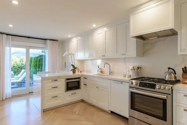 Kitchen featuring sink, white cabinets, premium range hood, light parquet flooring, and appliances with stainless steel finishes Kitchen featuring sink, white cabinets, premium range hood, light parquet flooring, and appliances with stainless steel finishes