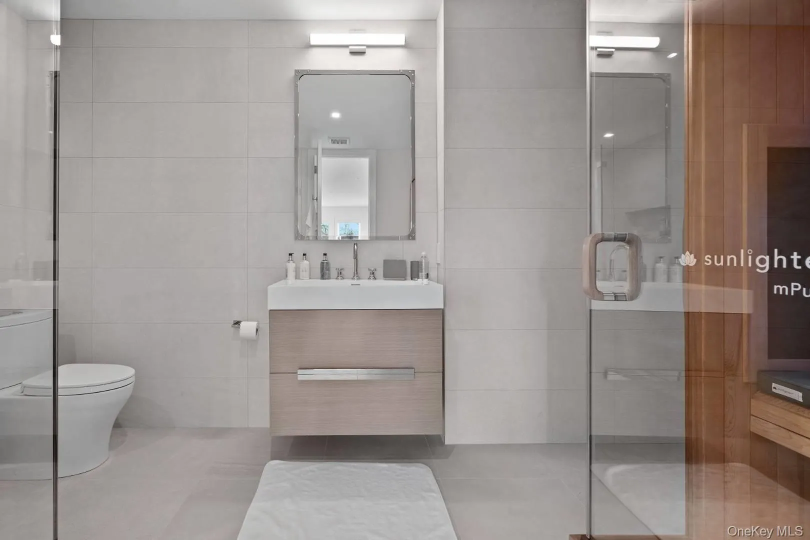 Bathroom featuring tile patterned floors, toilet, vanity, a shower with shower door, and tile walls Bathroom featuring tile patterned floors, toilet, vanity, a shower with shower door, and tile walls