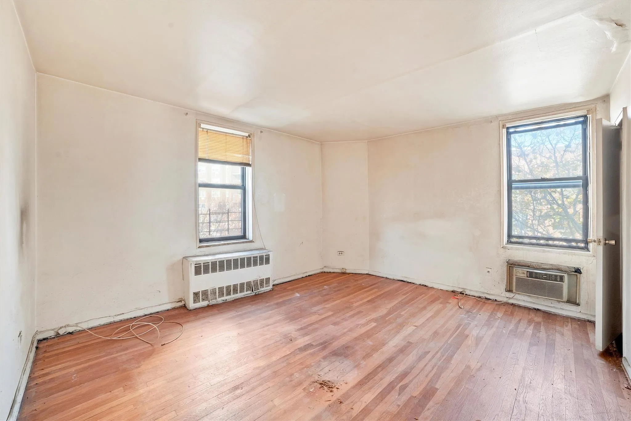 Empty room with an AC wall unit, radiator heating unit, and hardwood / wood-style floors Empty room with an AC wall unit, radiator heating unit, and hardwood / wood-style floors