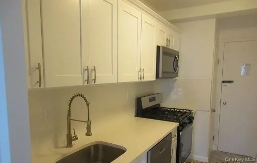 Kitchen featuring appliances with stainless steel finishes, tasteful backsplash, white cabinetry, and sink Kitchen featuring appliances with stainless steel finishes, tasteful backsplash, white cabinetry, and sink