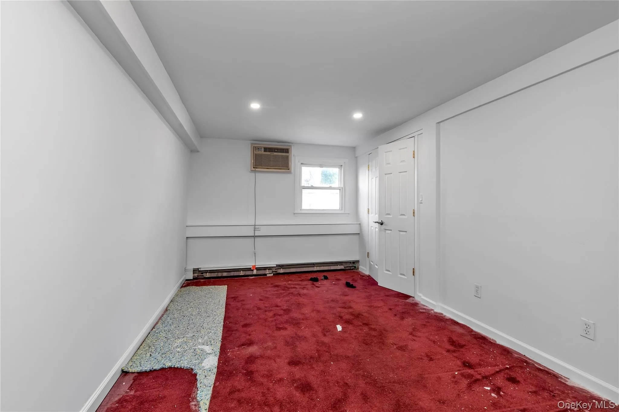 Carpeted empty room featuring an AC wall unit and a baseboard heating unit Carpeted empty room featuring an AC wall unit and a baseboard heating unit