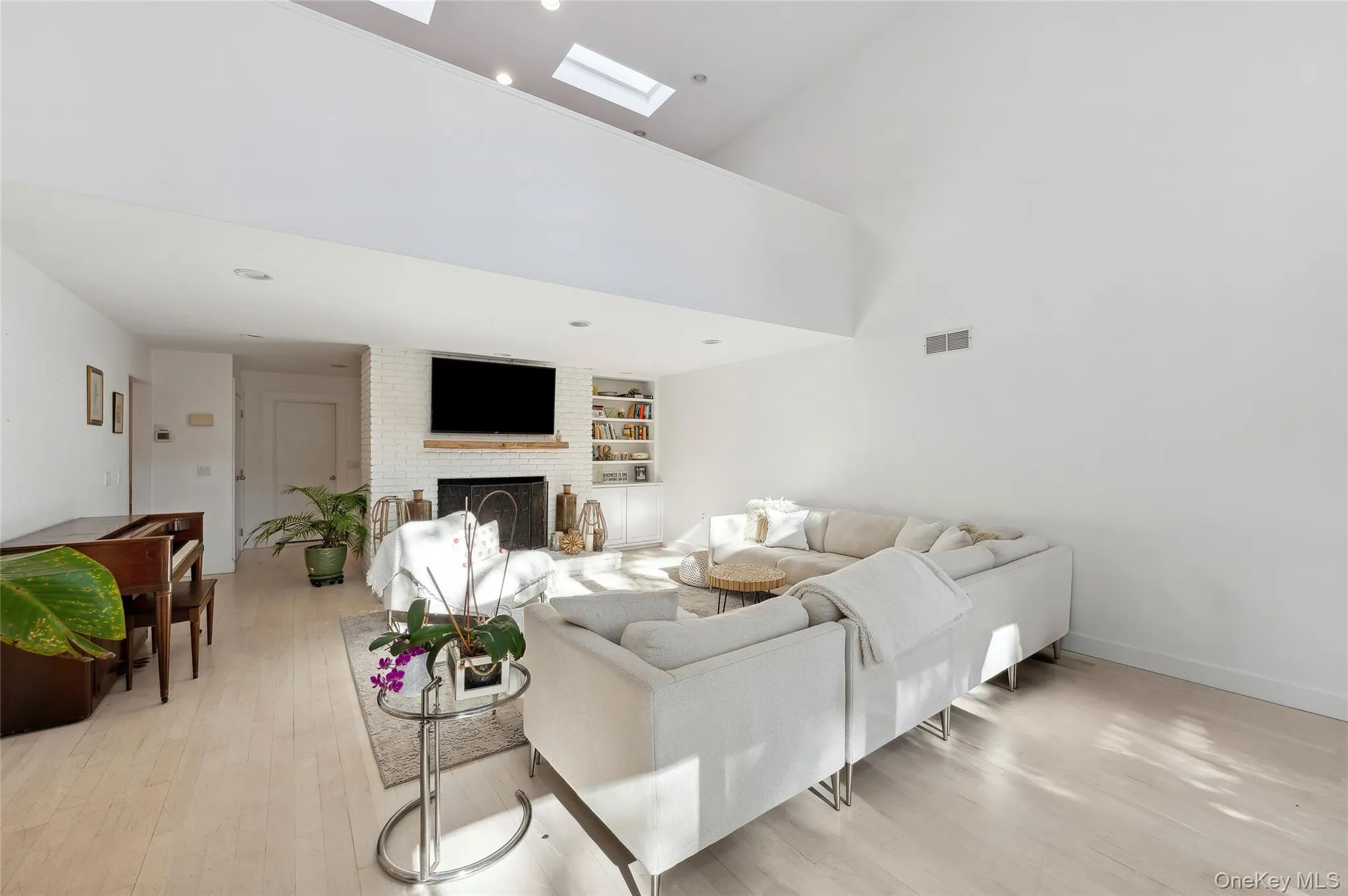 Living room featuring a high ceiling, light wood-type flooring, a skylight, and a brick fireplace Living room featuring a high ceiling, light wood-type flooring, a skylight, and a brick fireplace