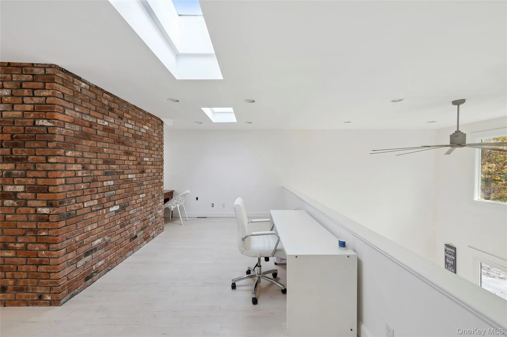 Unfurnished office featuring ceiling fan, light wood-type flooring, and brick wall Unfurnished office featuring ceiling fan, light wood-type flooring, and brick wall