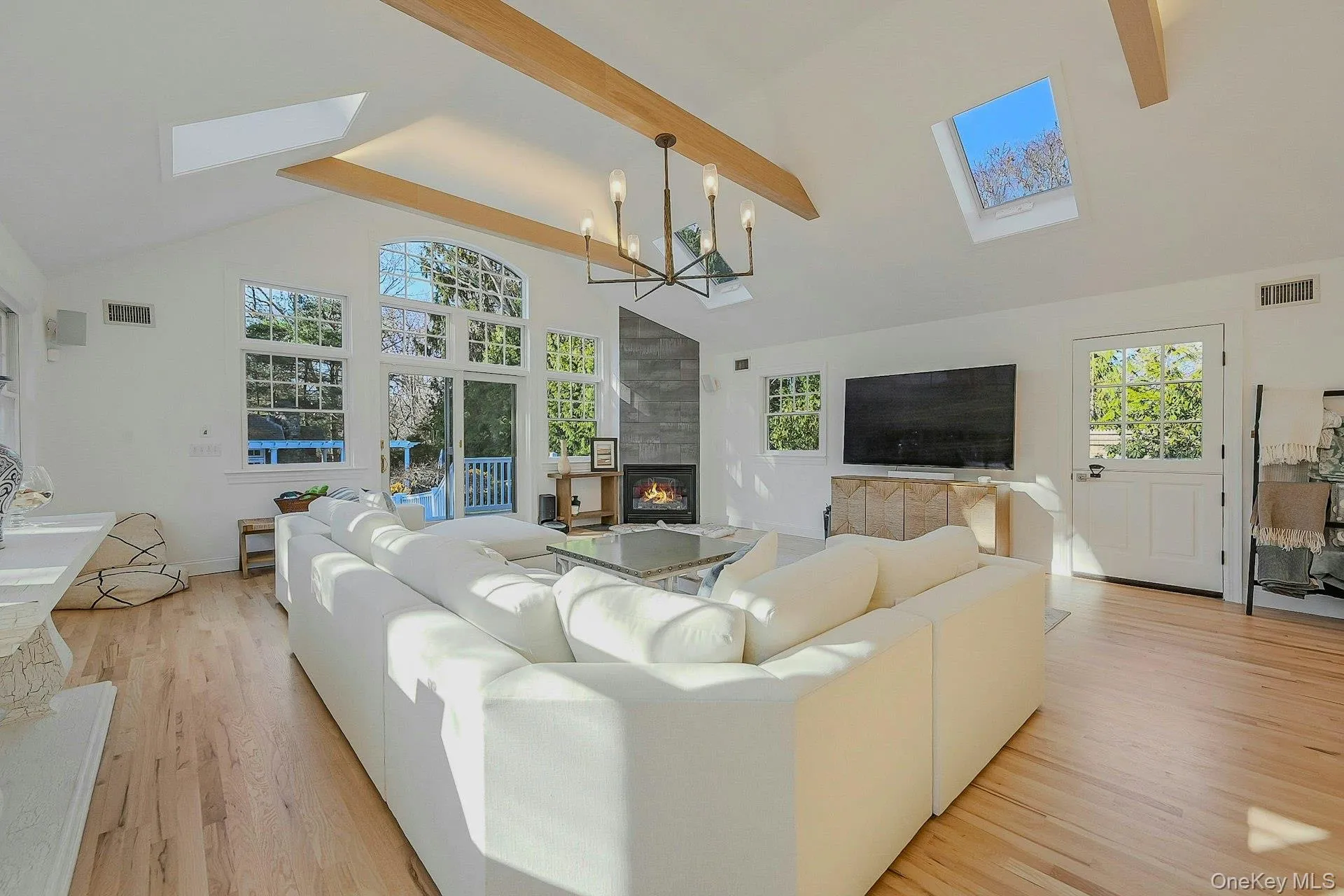 Living room featuring beamed ceiling, light hardwood / wood-style flooring, plenty of natural light, and a notable chandelier Living room featuring beamed ceiling, light hardwood / wood-style flooring, plenty of natural light, and a notable chandelier
