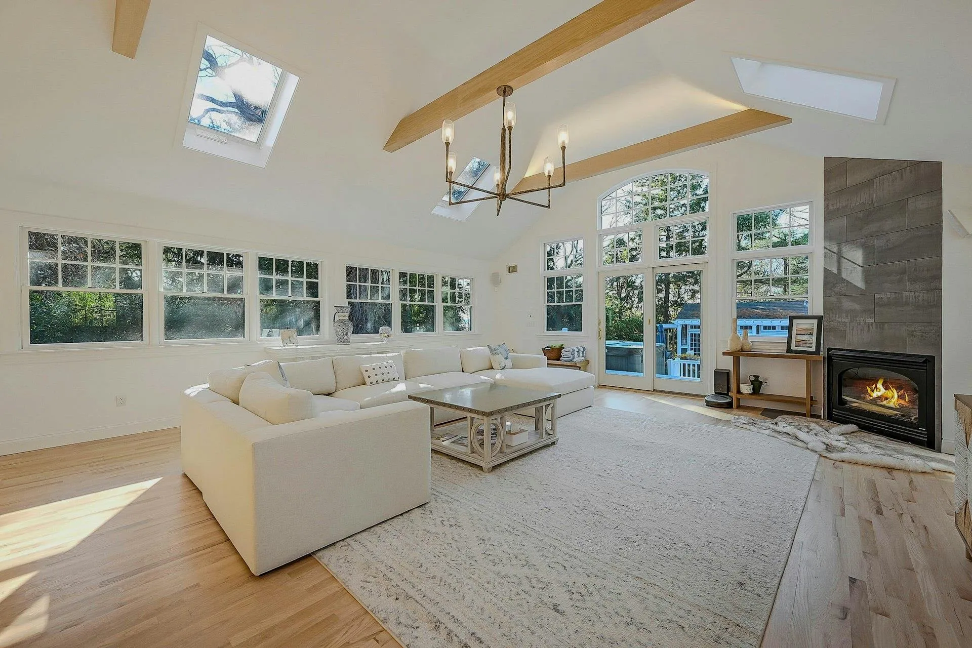 Living room with beamed ceiling, light hardwood / wood-style flooring, high vaulted ceiling, and a tiled fireplace Living room with beamed ceiling, light hardwood / wood-style flooring, high vaulted ceiling, and a tiled fireplace