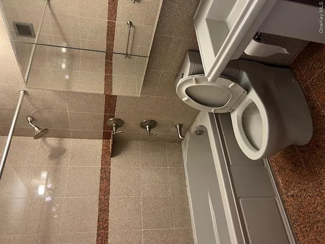 Bathroom featuring tiled shower / bath combo, toilet, and tile walls Bathroom featuring tiled shower / bath combo, toilet, and tile walls