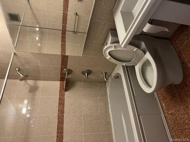 Bathroom featuring tiled shower / bath combo, toilet, and tile walls Bathroom featuring tiled shower / bath combo, toilet, and tile walls