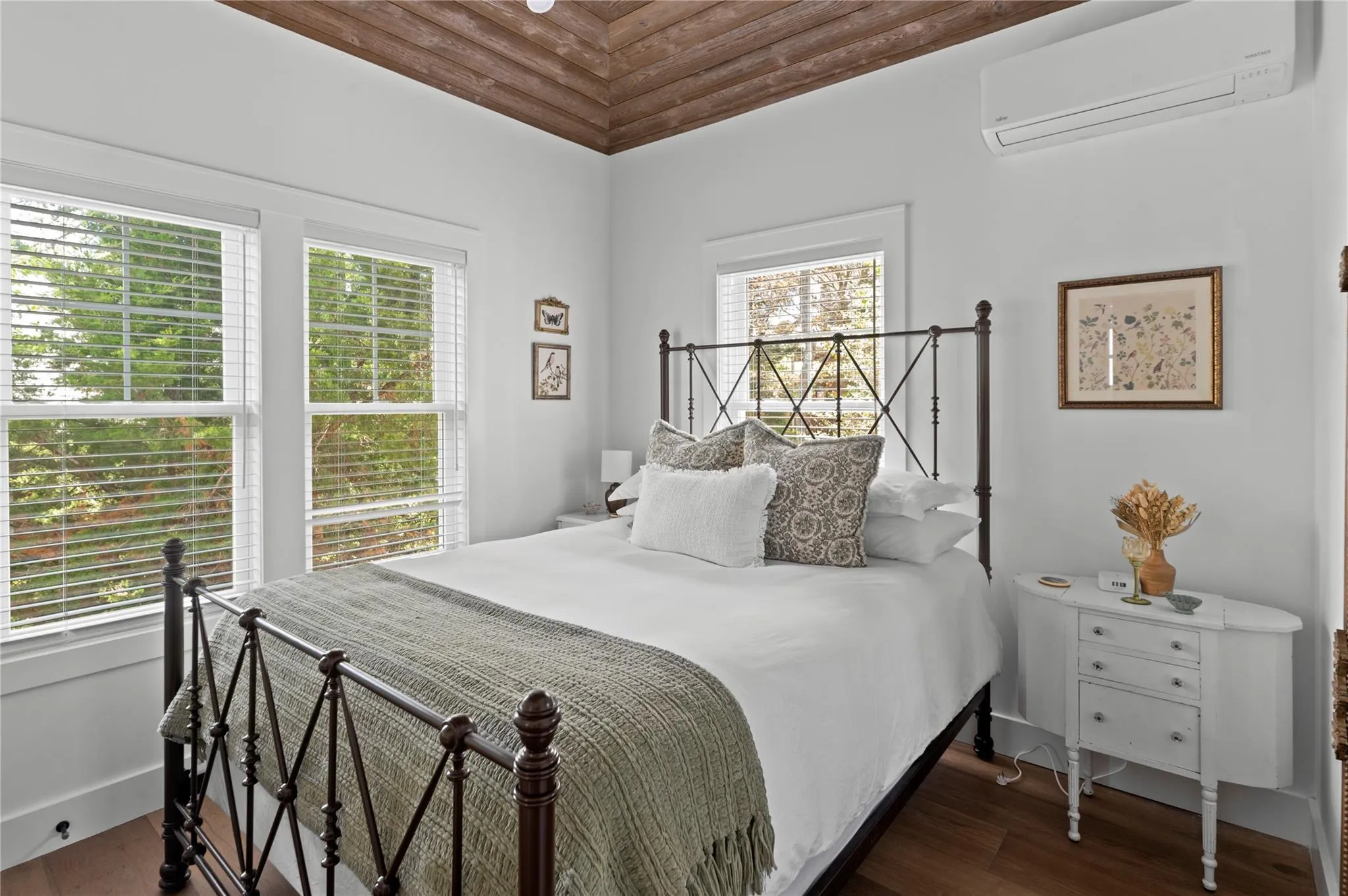 Bedroom with an AC wall unit, multiple windows, and wood finished floors Bedroom with an AC wall unit, multiple windows, and wood finished floors
