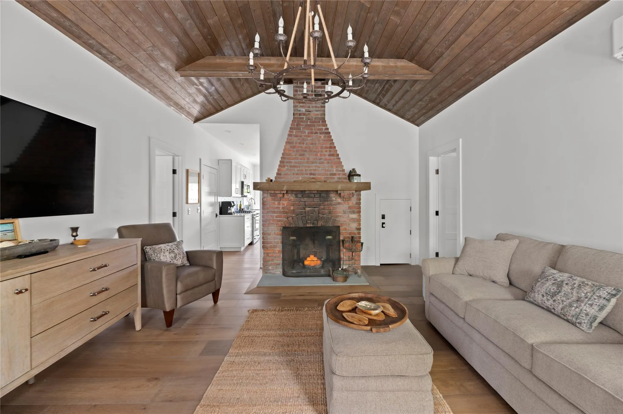 Living room with wood ceiling, a chandelier, high vaulted ceiling, wood finished floors, and a brick fireplace Living room with wood ceiling, a chandelier, high vaulted ceiling, wood finished floors, and a brick fireplace