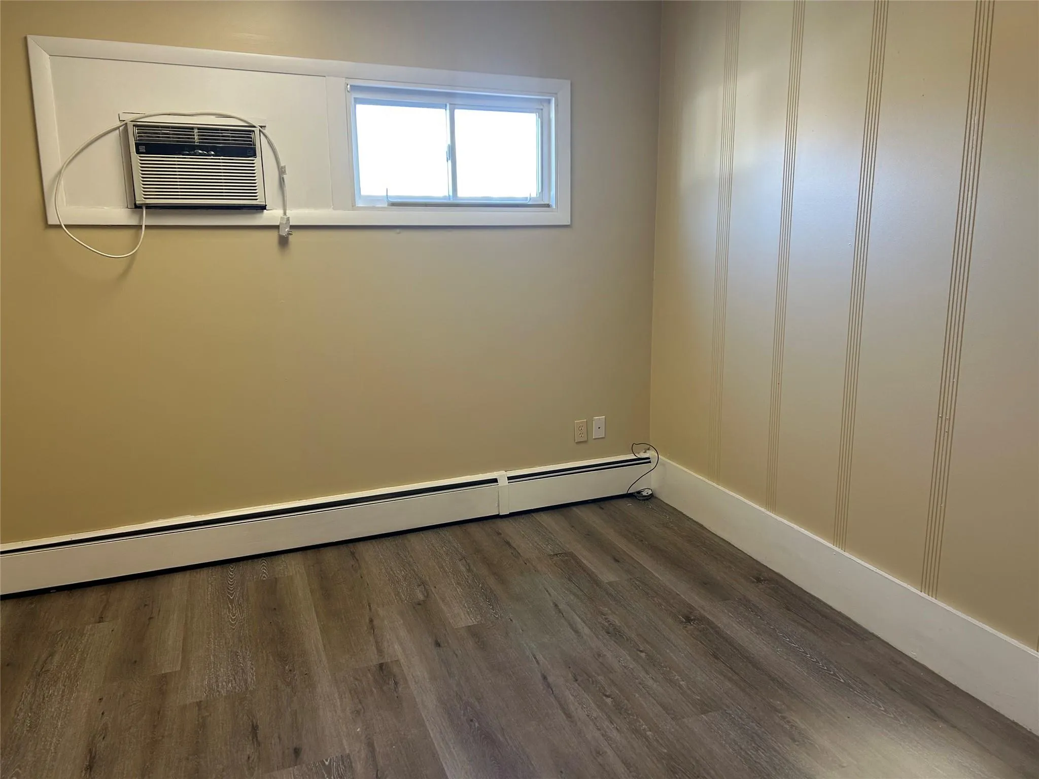 Empty room featuring a wall mounted air conditioner, dark hardwood / wood-style flooring, and a baseboard radiator Empty room featuring a wall mounted air conditioner, dark hardwood / wood-style flooring, and a baseboard radiator