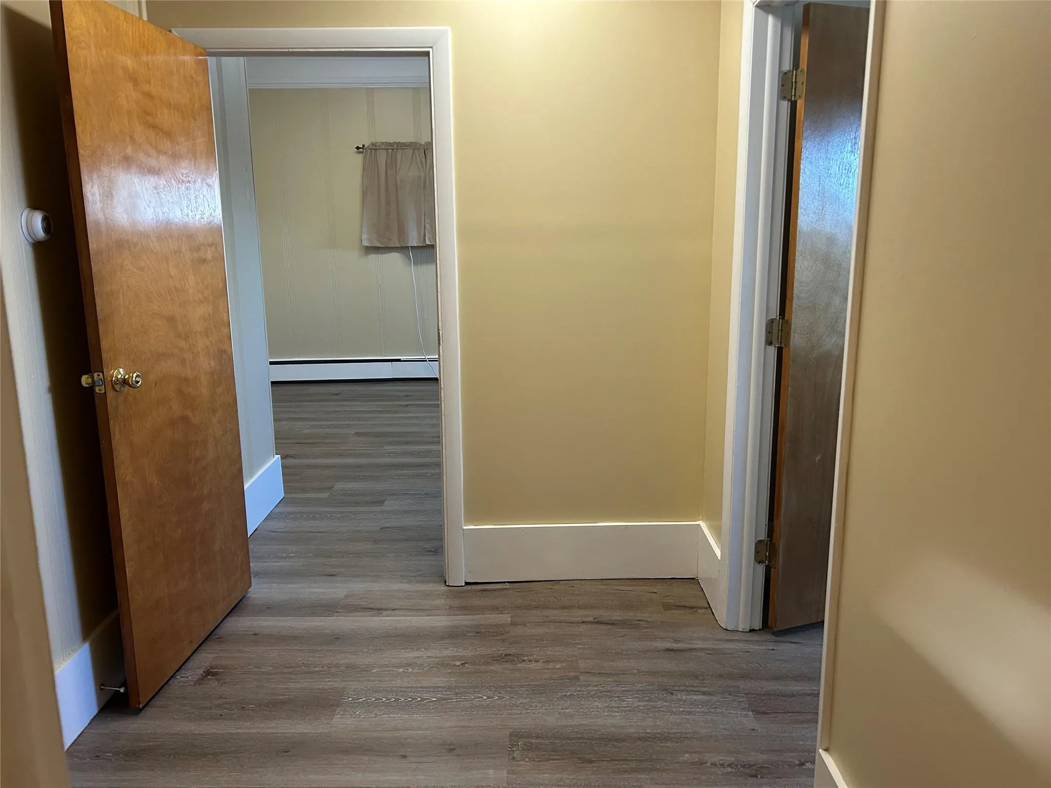 Hallway featuring wood-type flooring and a baseboard heating unit Hallway featuring wood-type flooring and a baseboard heating unit