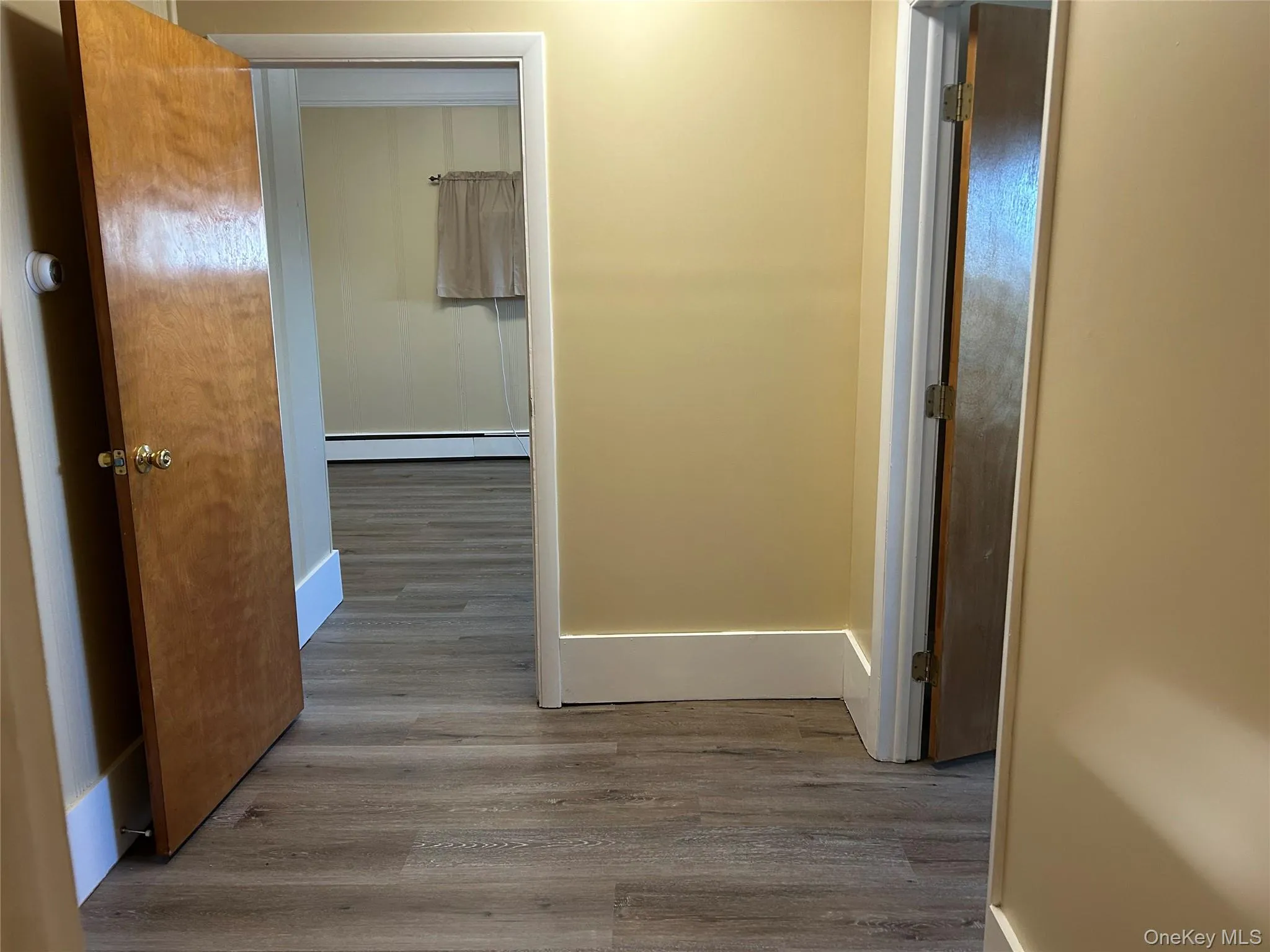 Hallway featuring wood-type flooring and a baseboard heating unit Hallway featuring wood-type flooring and a baseboard heating unit