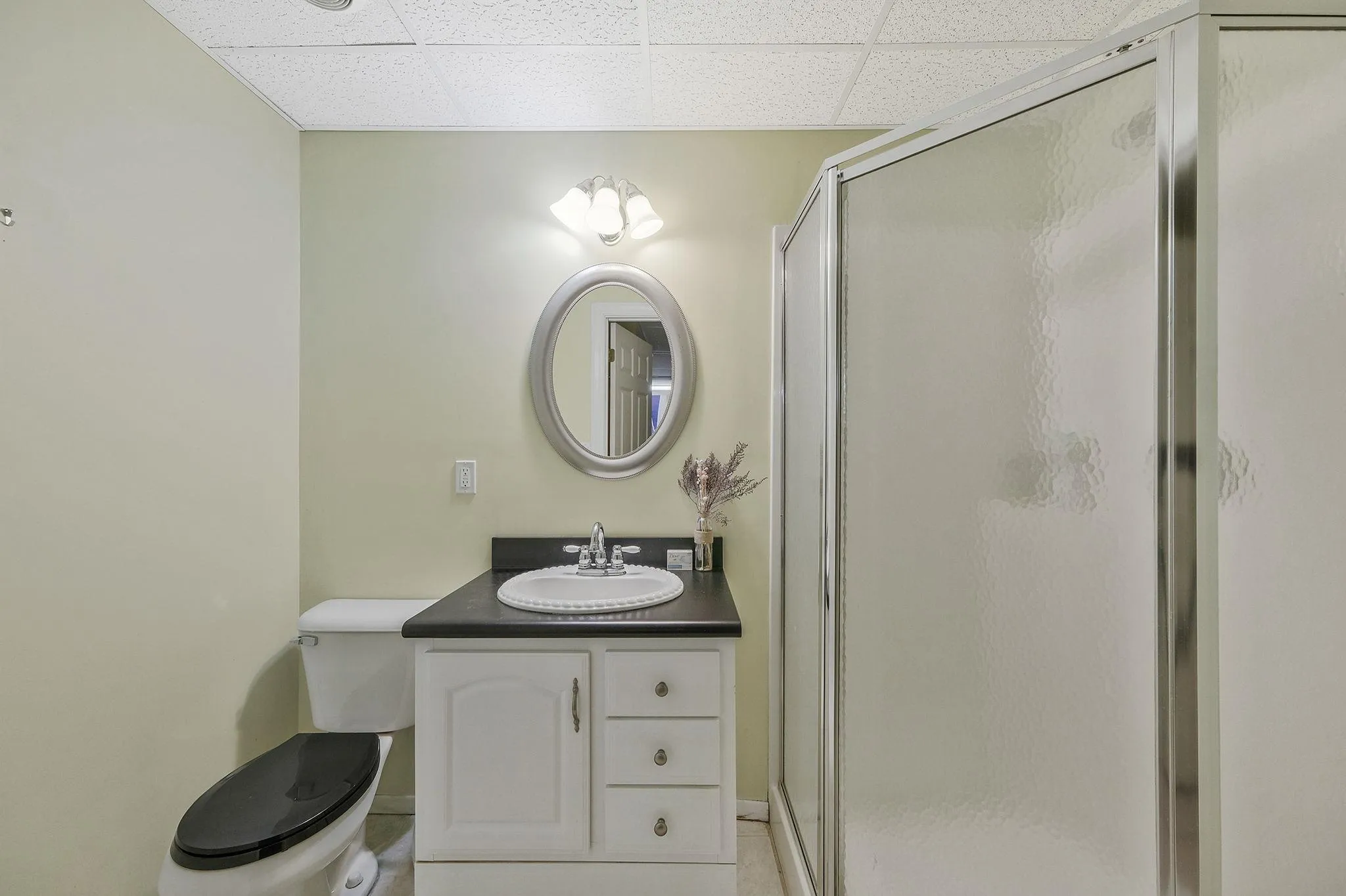 Bathroom featuring a drop ceiling, tile patterned flooring, toilet, vanity, and a shower with shower door Bathroom featuring a drop ceiling, tile patterned flooring, toilet, vanity, and a shower with shower door