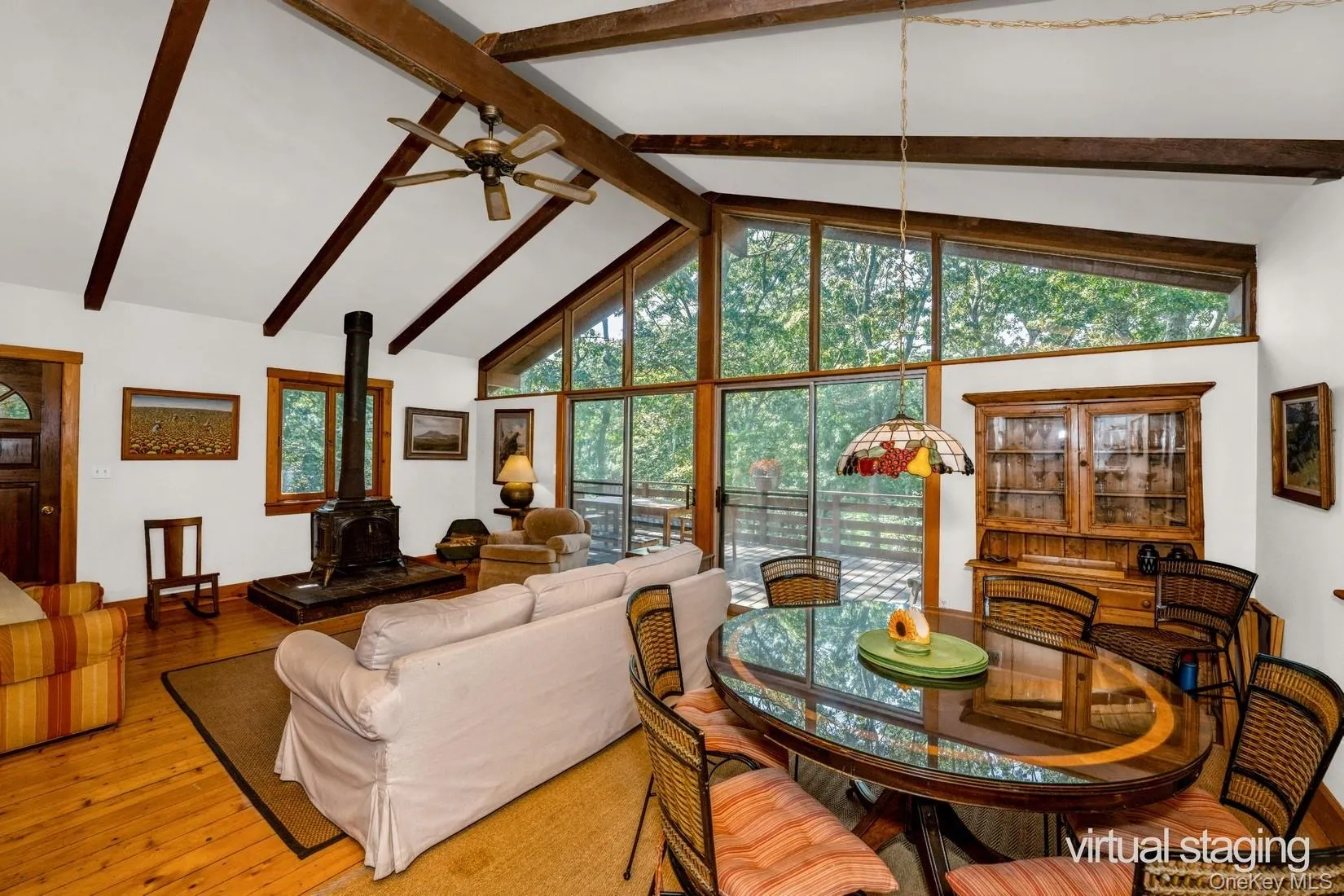 Living area featuring beam ceiling, light wood-style flooring, a wood stove, and ceiling fan