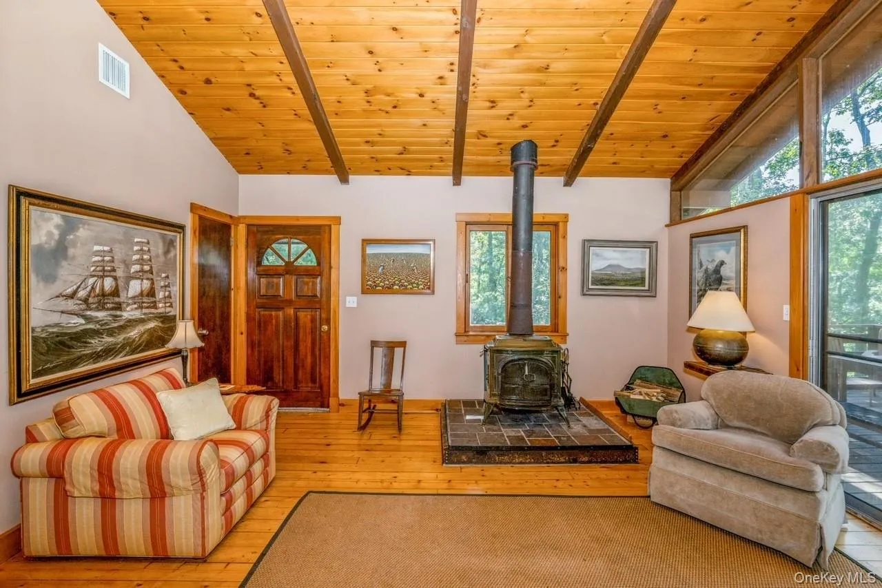 Living room featuring a wood stove, high ceiling with beams, light hardwood / wood-style flooring, and wooden ceiling