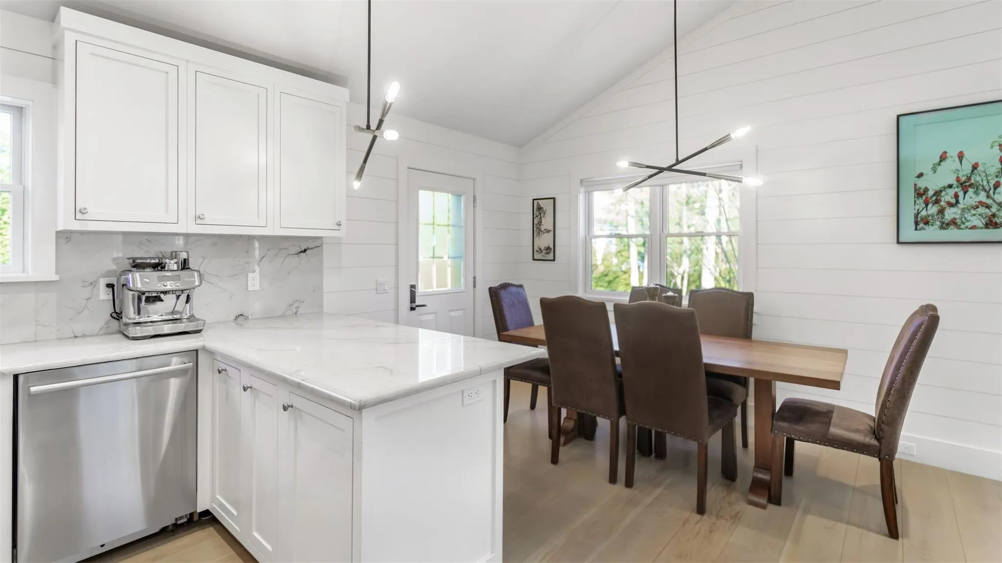 Kitchen featuring stainless steel dishwasher, vaulted ceiling, decorative light fixtures, light hardwood / wood-style floors, and white cabinetry Kitchen featuring stainless steel dishwasher, vaulted ceiling, decorative light fixtures, light hardwood / wood-style floors, and white cabinetry