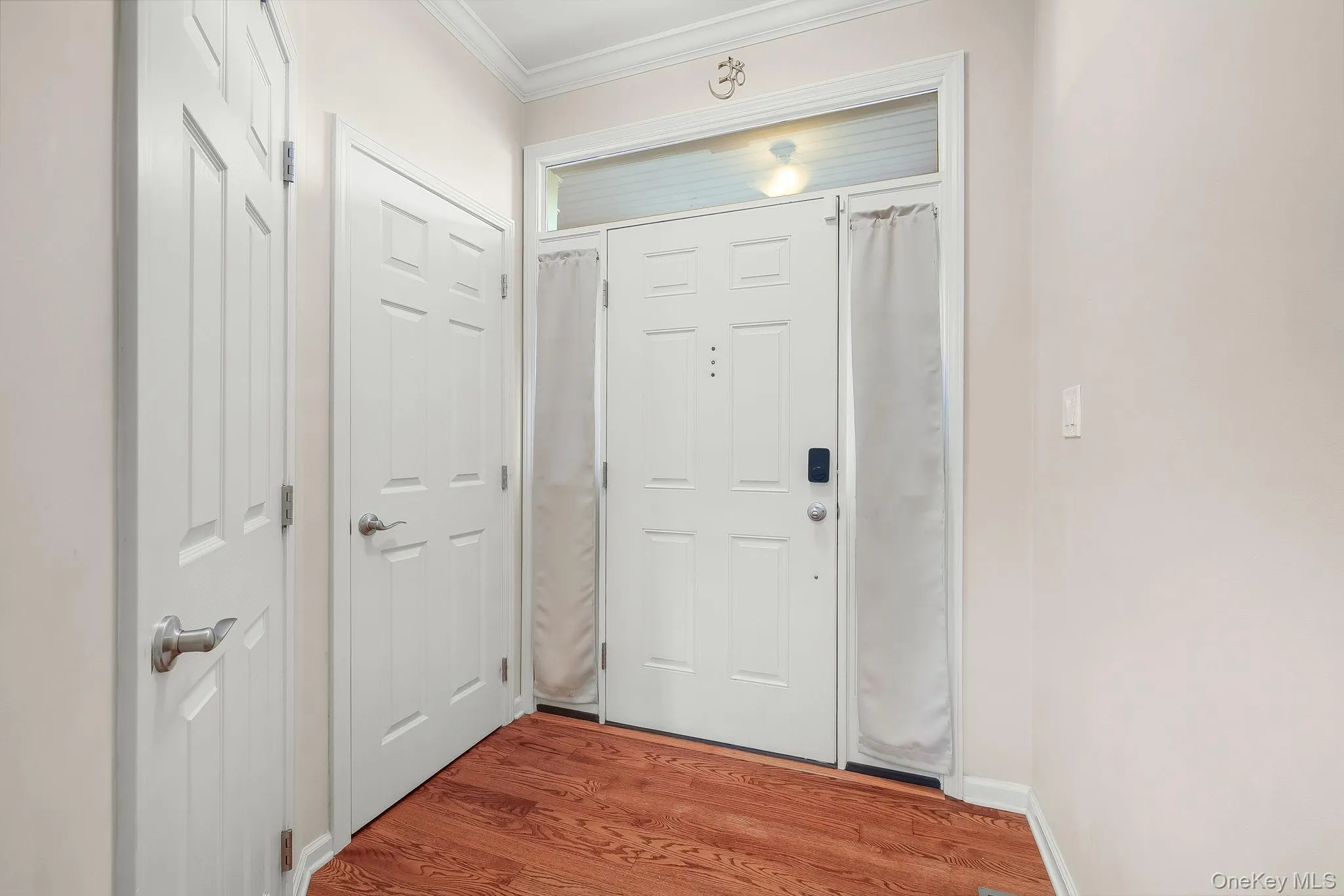 Entryway featuring rich wood-finish flooring, white panel doors, and crown molding Entryway featuring rich wood-finish flooring, white panel doors, and crown molding