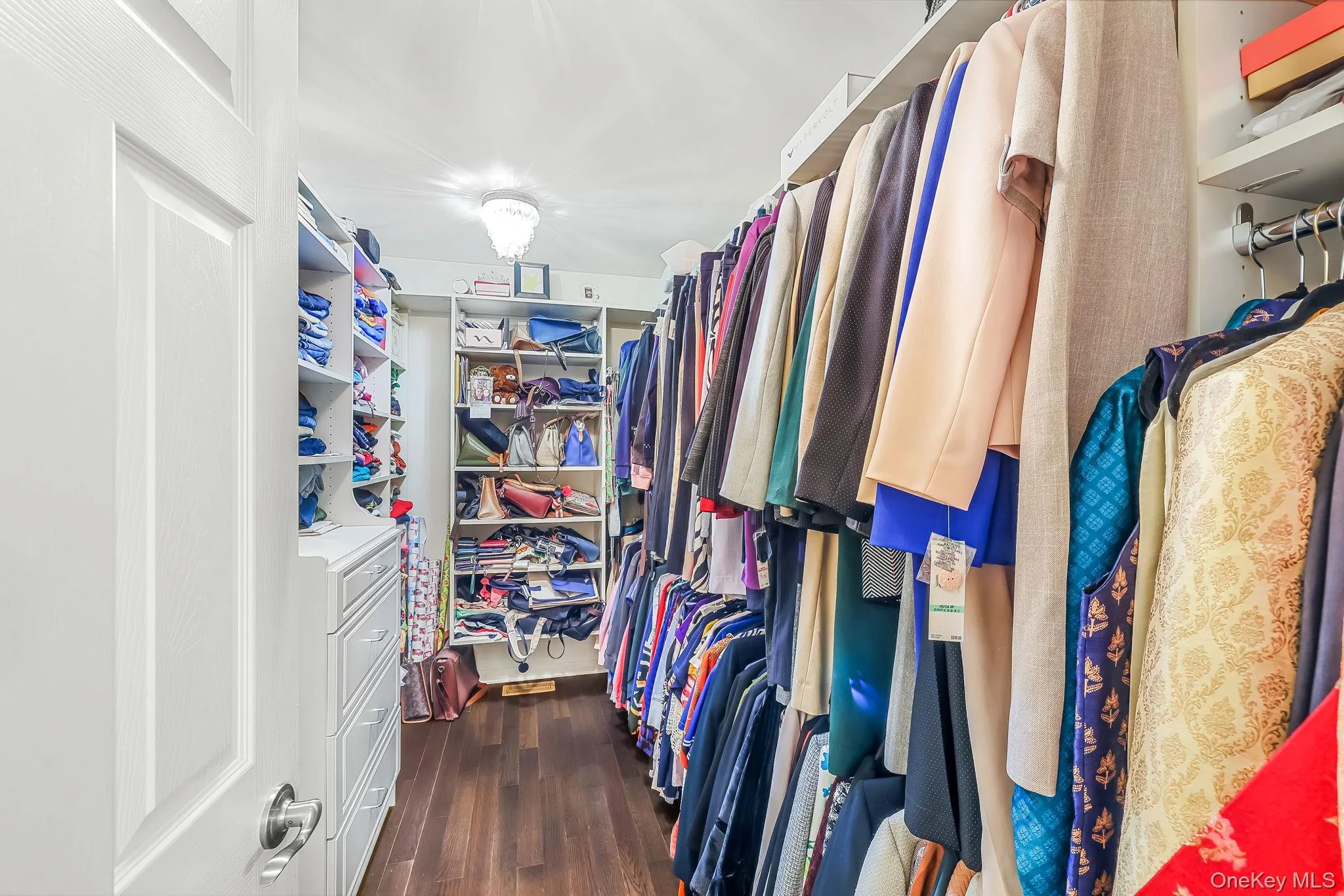 Walk-in closet with extensive built-in shelving, rich wood-finish flooring, and a decorative ceiling light fixture Walk-in closet with extensive built-in shelving, rich wood-finish flooring, and a decorative ceiling light fixture