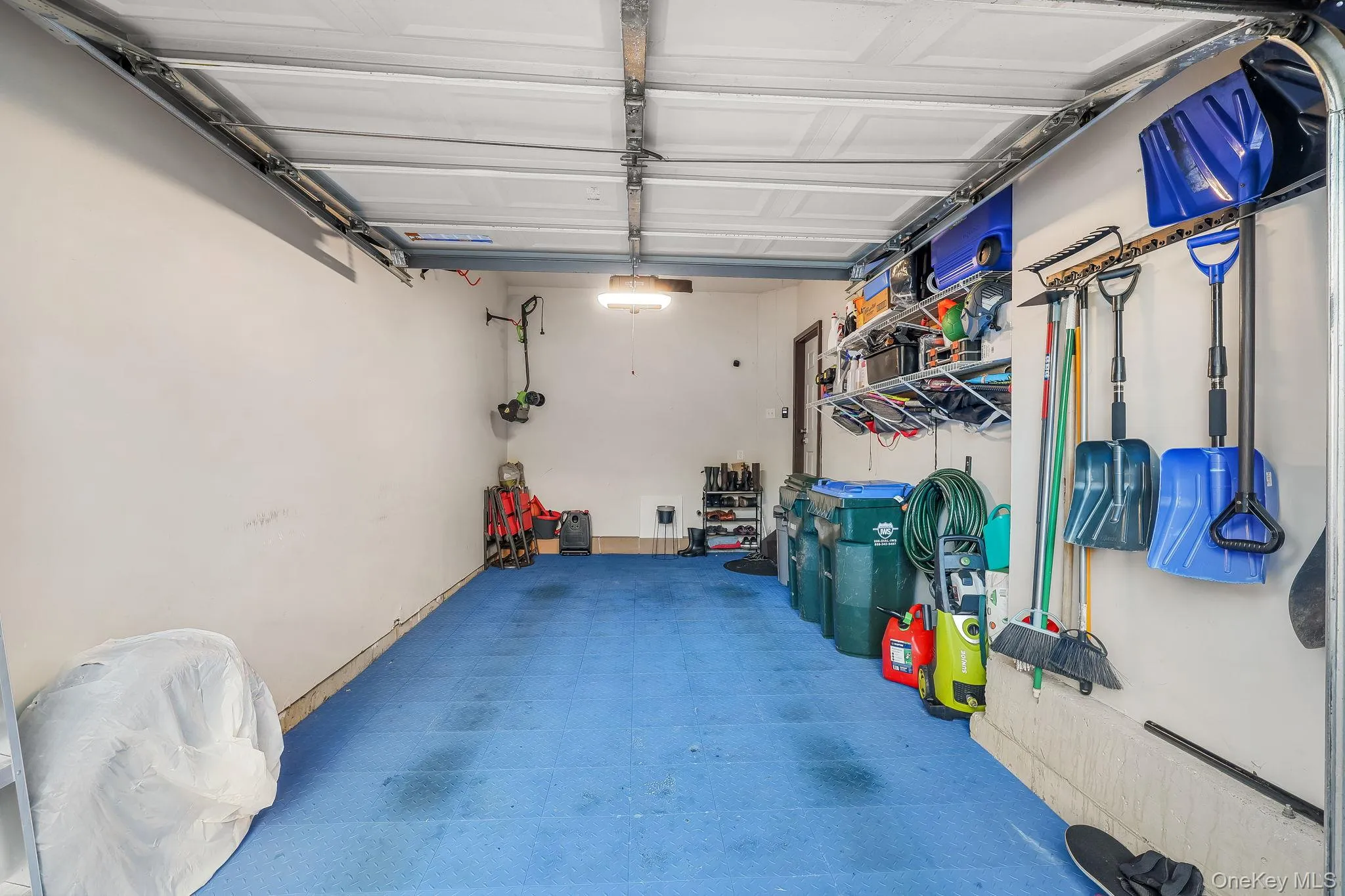 Attached garage with an overhead door, blue floor surfacing, recessed lighting, and wall-mounted shelving Attached garage with an overhead door, blue floor surfacing, recessed lighting, and wall-mounted shelving