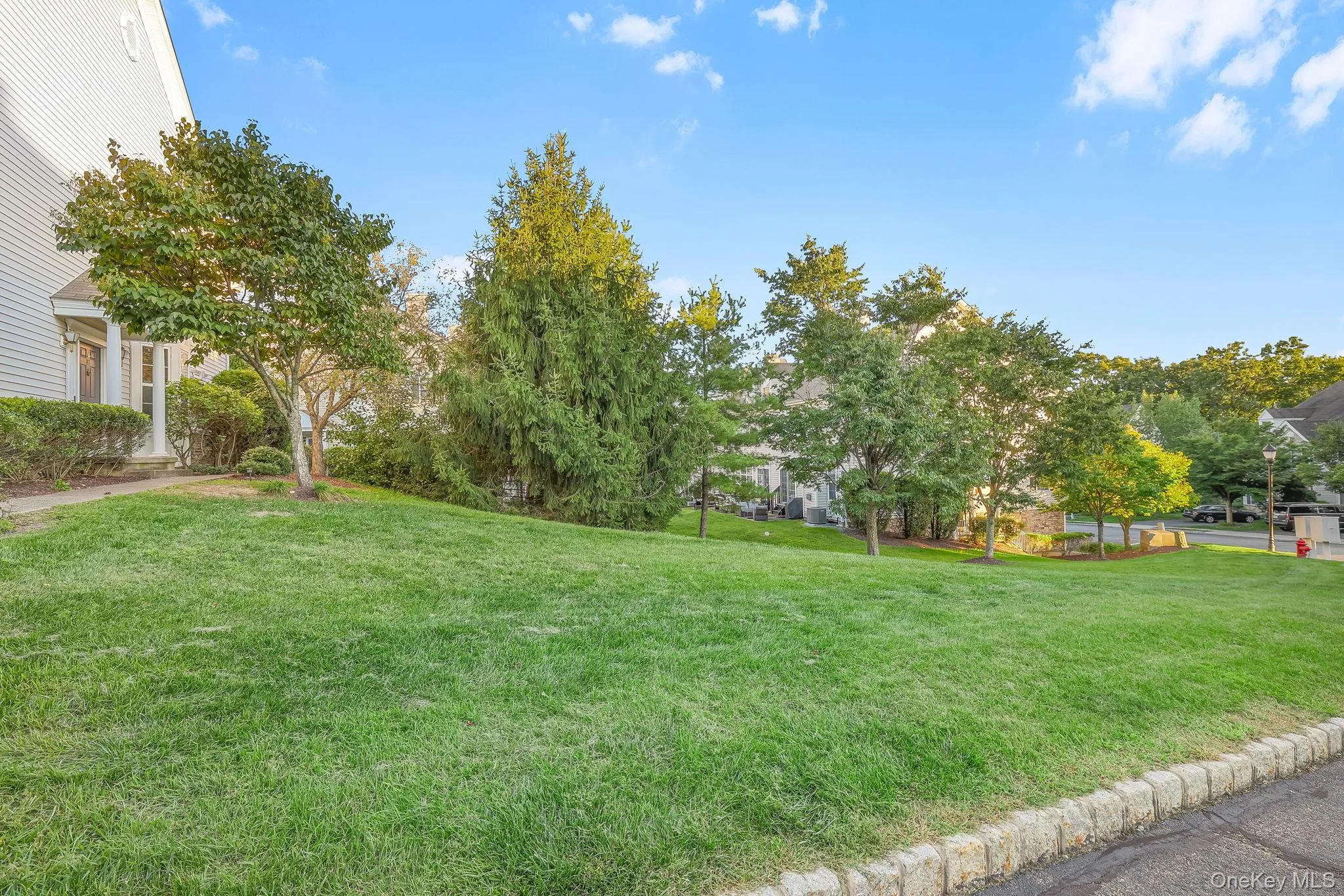 Directly across from the home with view of open expansive lawn area with mature trees and shrubbery, bordered by a stone curb Directly across from the home with view of open expansive lawn area with mature trees and shrubbery, bordered by a stone curb