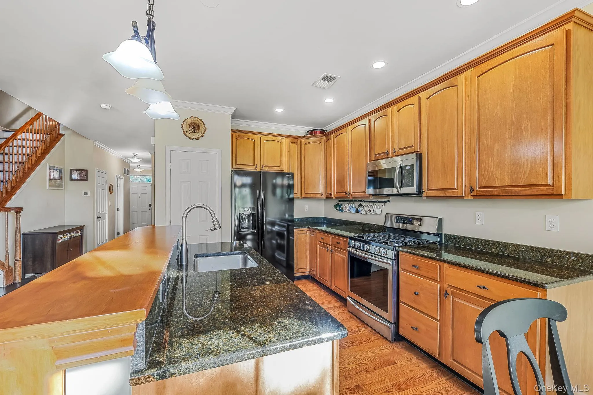 Kitchen featuring wood cabinetry, stainless steel appliances, dark stone countertops, wood-finish flooring, and a stainless steel sink with a gooseneck faucet Kitchen featuring wood cabinetry, stainless steel appliances, dark stone countertops, wood-finish flooring, and a stainless steel sink with a gooseneck faucet