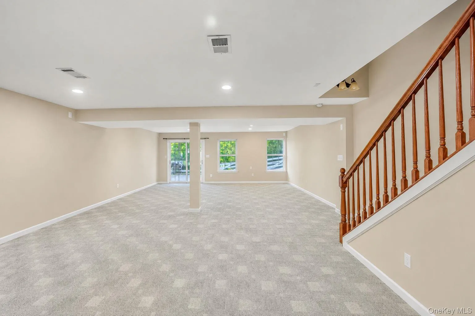AI showing the removal of gym/furniture. Expansive finished interior space with patterned carpet flooring, recessed lighting, and a wood-finish staircase AI showing the removal of gym/furniture. Expansive finished interior space with patterned carpet flooring, recessed lighting, and a wood-finish staircase