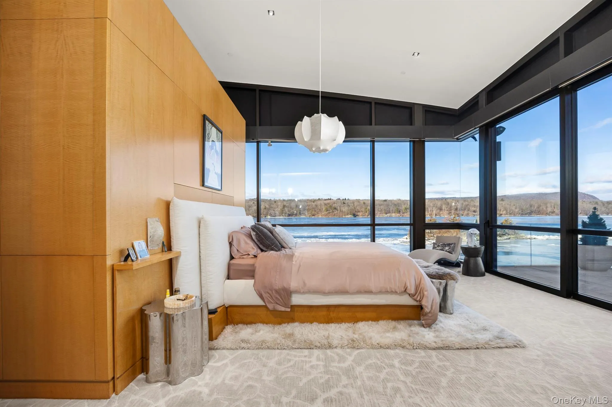 Carpeted bedroom with access to exterior, a water view, a wall of windows, and wooden walls Carpeted bedroom with access to exterior, a water view, a wall of windows, and wooden walls
