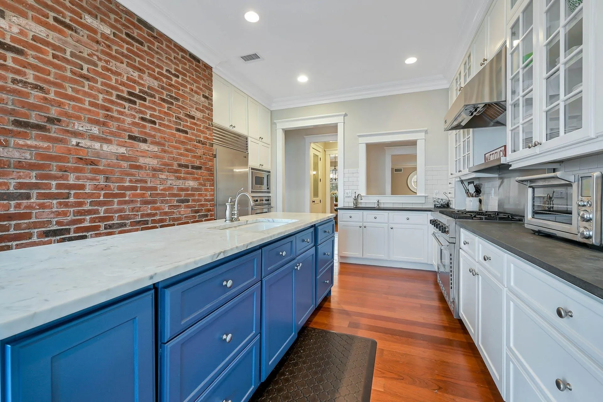Kitchen with dark hardwood / wood-style flooring, backsplash, brick wall, blue cabinets, and built in appliances Kitchen with dark hardwood / wood-style flooring, backsplash, brick wall, blue cabinets, and built in appliances