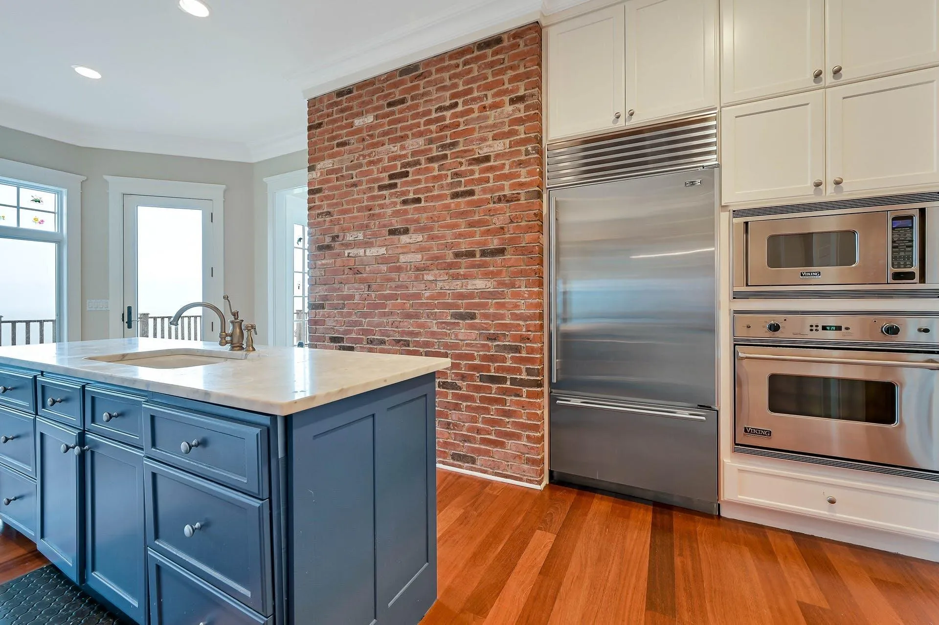 Kitchen featuring ornamental molding, brick wall, blue cabinets, sink, and built in appliances Kitchen featuring ornamental molding, brick wall, blue cabinets, sink, and built in appliances