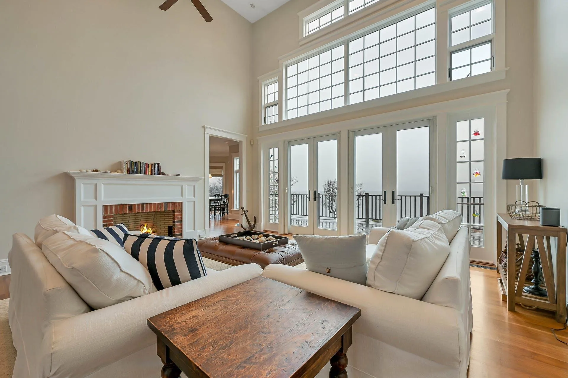 Living room with french doors, ceiling fan, light wood-type flooring, a towering ceiling, and a fireplace Living room with french doors, ceiling fan, light wood-type flooring, a towering ceiling, and a fireplace