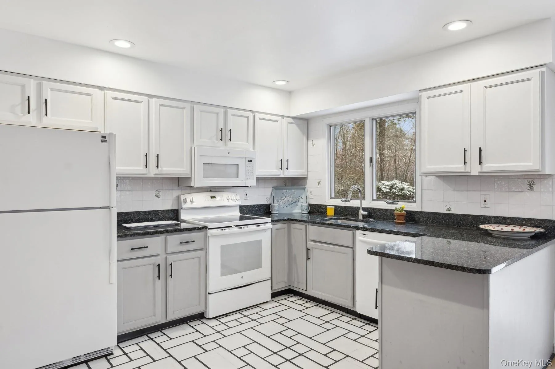Kitchen with backsplash, white appliances, sink, dark stone countertops, and white cabinetry Kitchen with backsplash, white appliances, sink, dark stone countertops, and white cabinetry